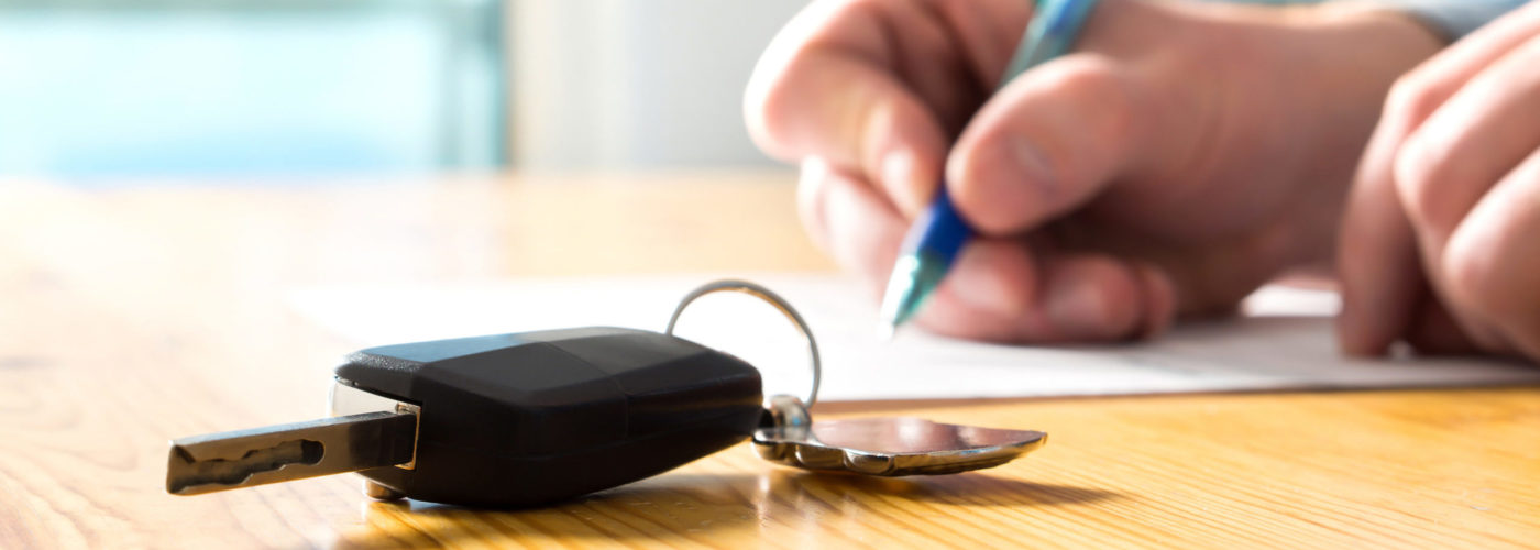 Close up of person signing documents in the background with a key to a rental car in the foreground