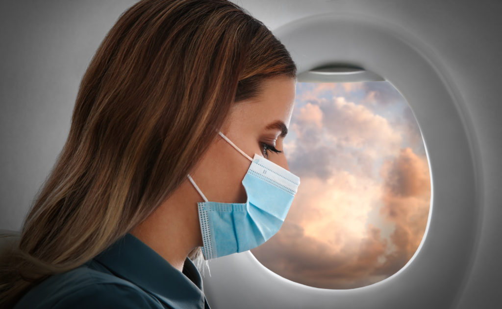 Woman wearing a mask next to a window on a plane at sunset