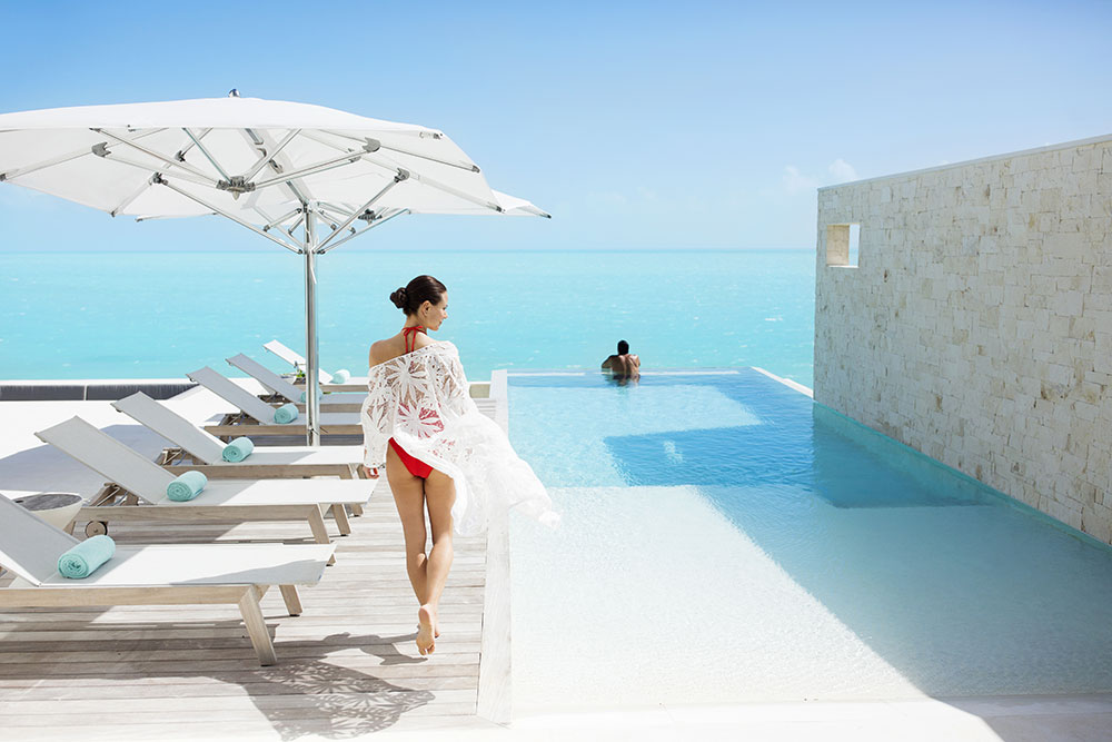 Woman walking towards man in infinity pool overlooking ocean at Wymara Villas in Turks and Caicos