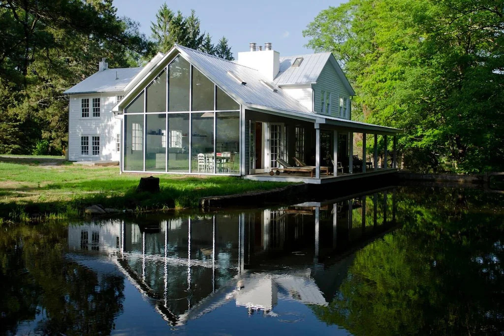 White farmhouse featuring large glass wall overlooking a lake