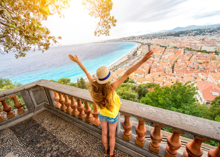 Woman with her arms raised on balcony overlooking Nice, France on a sunny day