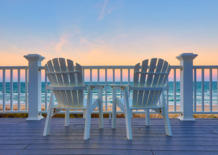 Adirondack chairs on a deck overlooking the ocean at sunset