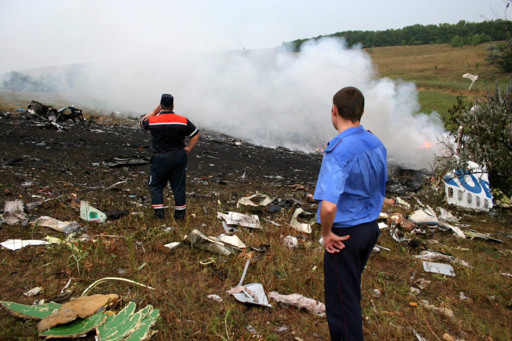 Two emergency responders looking at the smoking wreckage of a plane crash