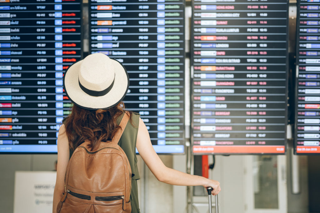 Woman holding rolling luggage and looking at a departures board in an airport