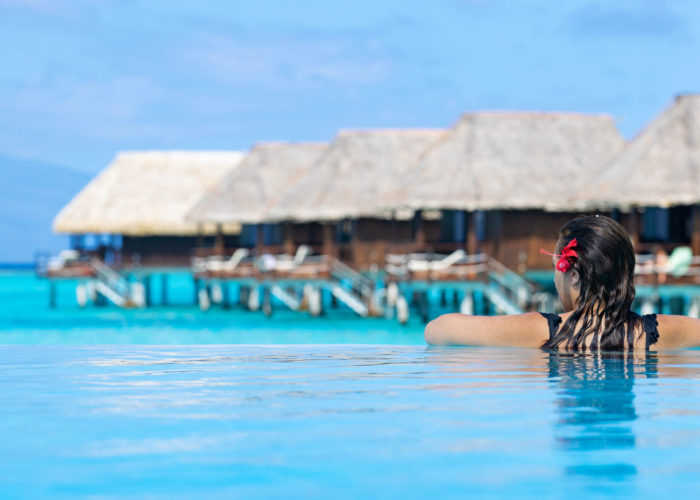 Woman in swimming pool overlooking a line of overwater bungalows