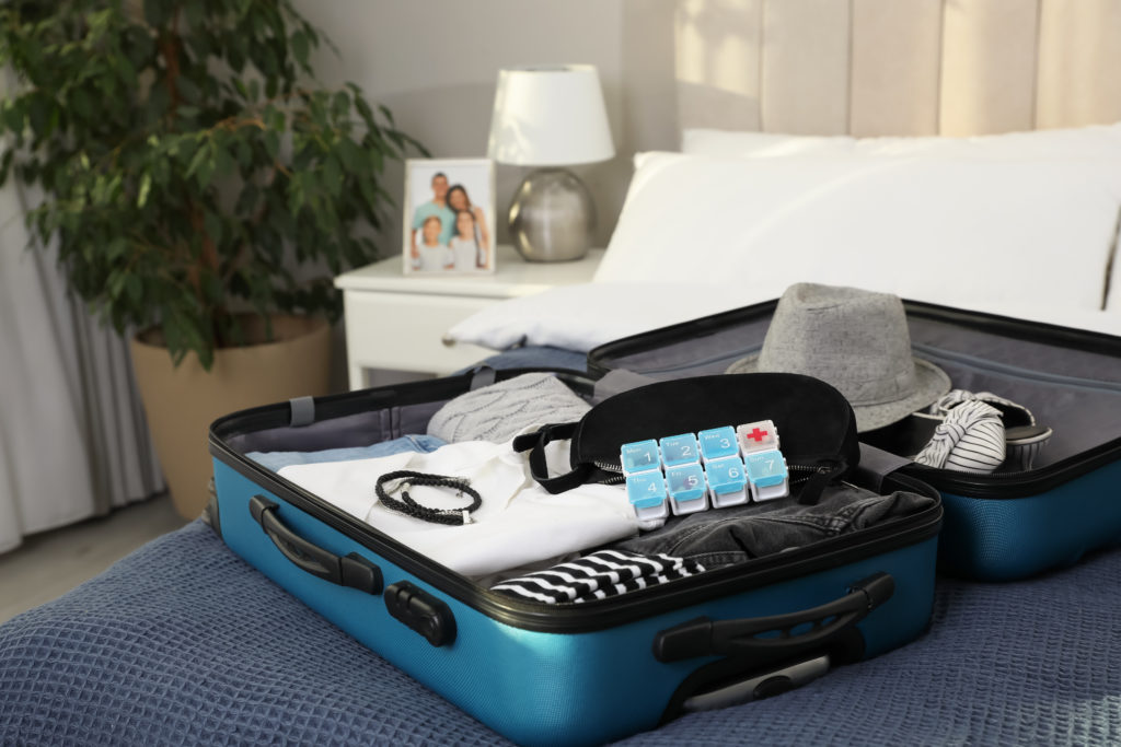 Open suitcase on bed full of clothes with a daily pill counter container on top