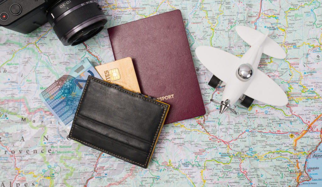 Passport, money, credit cards, model plane, and camera on top of a map