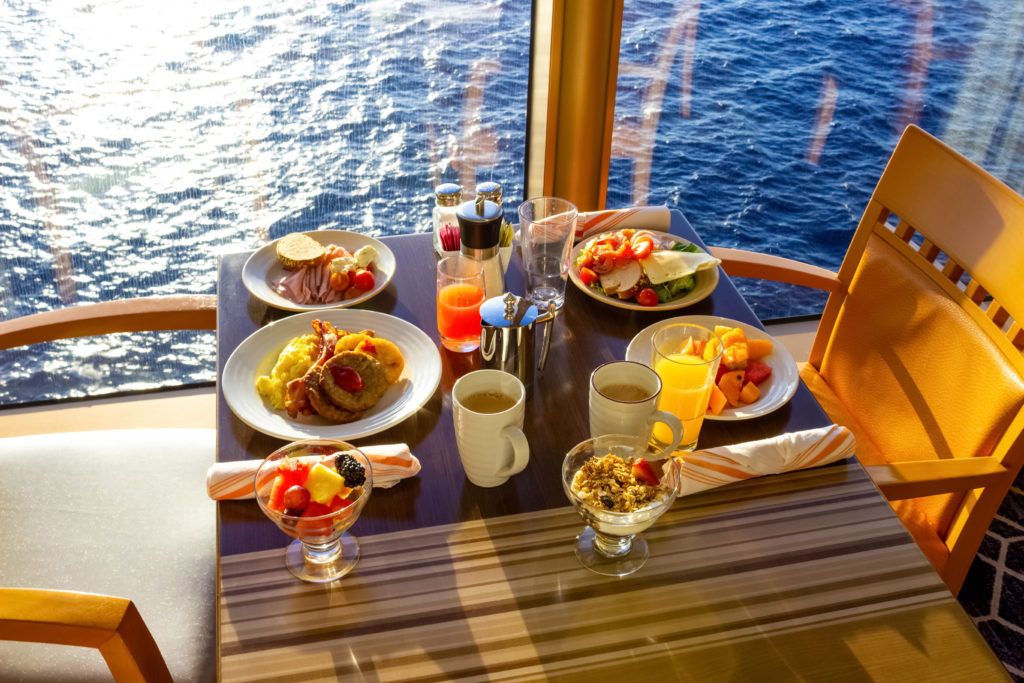 Full breakfast table in front of an ocean view window on a cruise
