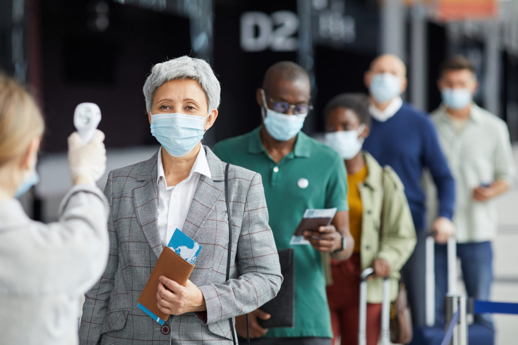 Group of masked people waiting in line at the airport to have their temperature taken