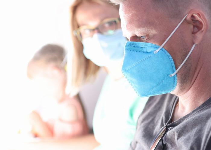 Man sits on airplane wearing a medical face mask with woman and child sitting next to him in the same row, out of focus