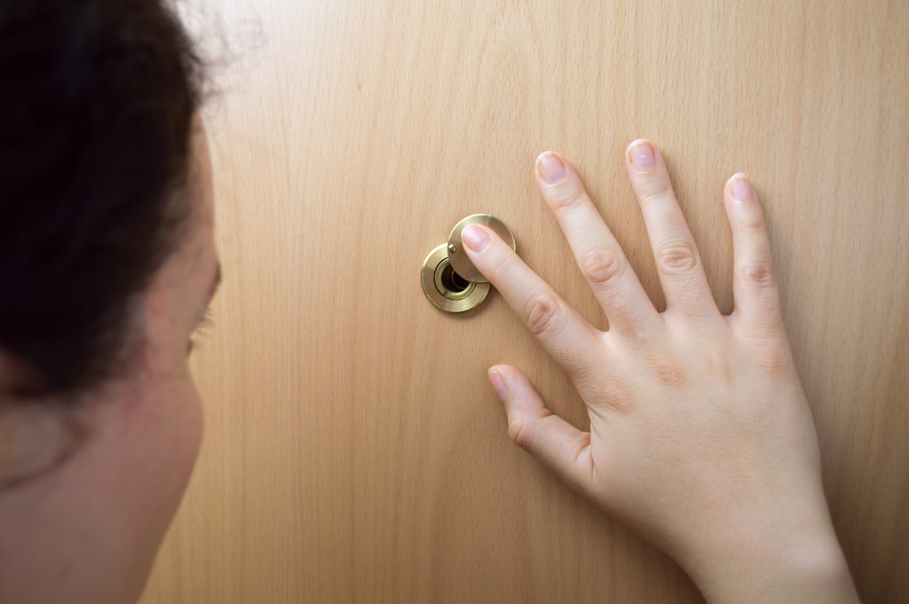 Woman looking through peephole in wooden door
