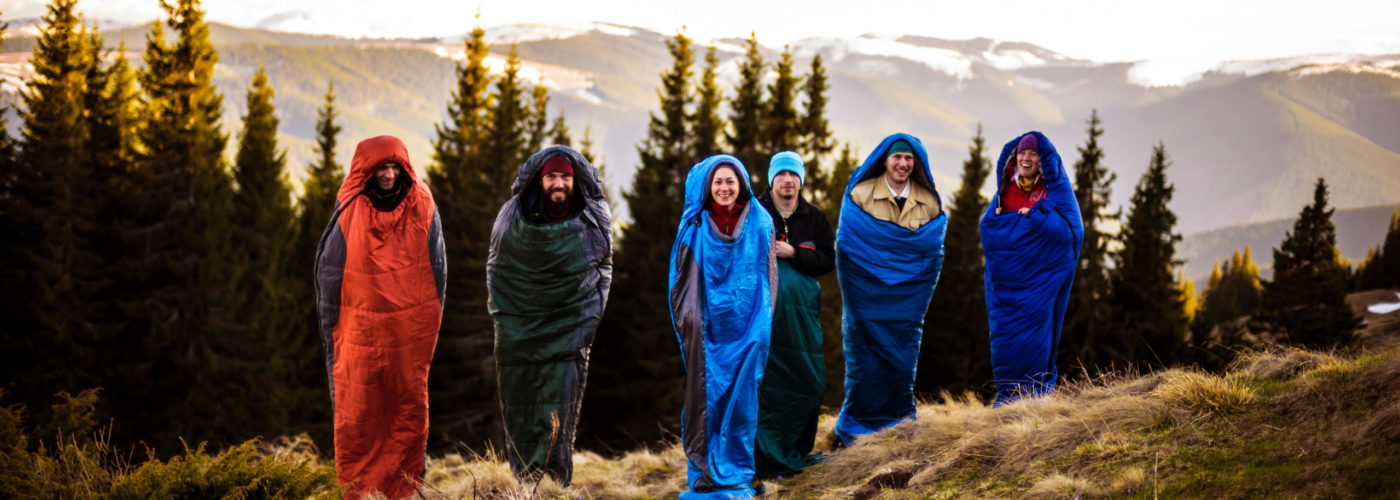 Group of people jumping in sleeping bags on a tree lined hill