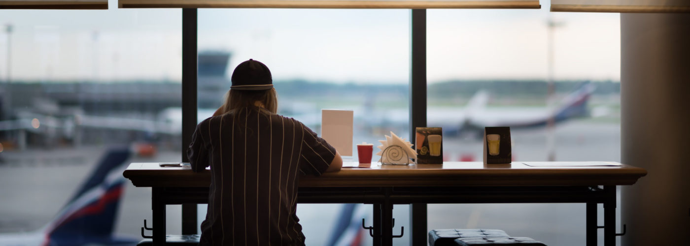 Person sitting at an airport cafe looking out the window at the airplanes on the runway