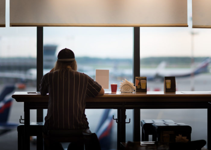 Person sitting at an airport cafe looking out the window at the airplanes on the runway