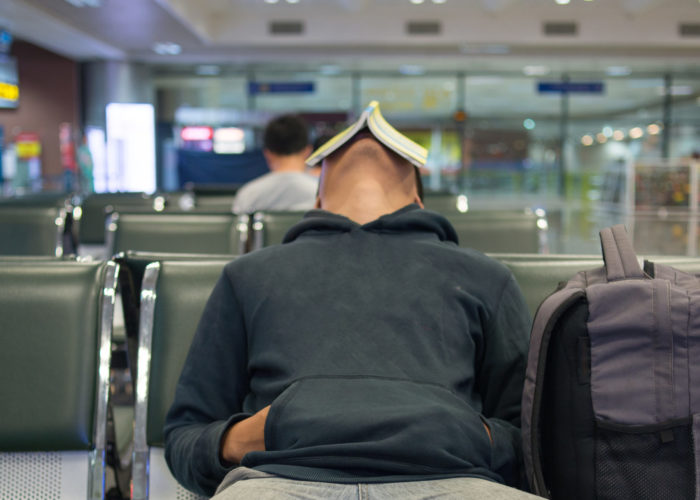 Person sleeping in airpot with a book propped on their face