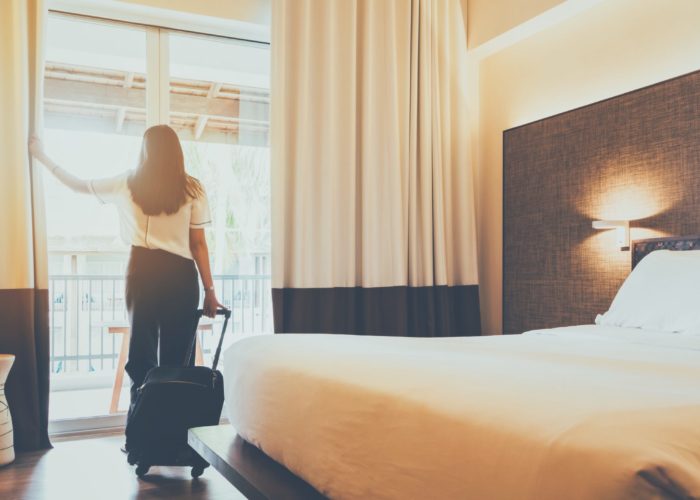 Woman pulling a rolling suitcase, looking out the window of her hotel room