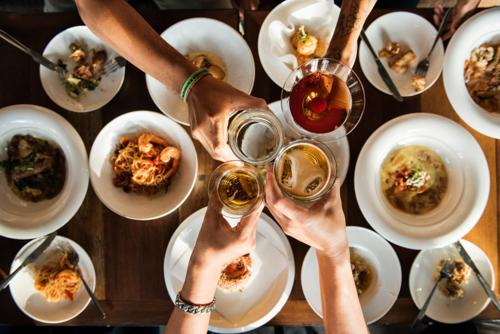 Bird's eye view of people clinking drinking glasses together over a table full of food