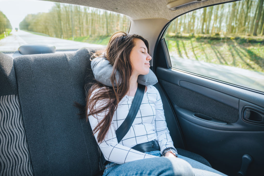 Woman sleeping in the backseat of a car using an airplane neck pillow
