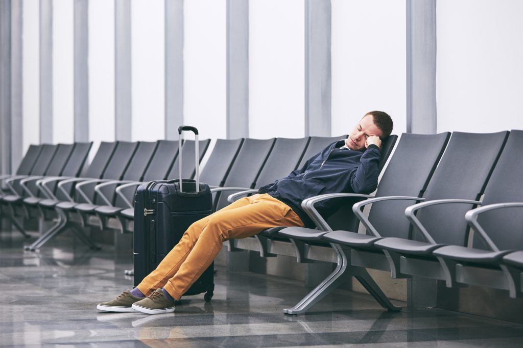 Man sleeping next to his rolling luggage in an empty airport terminal