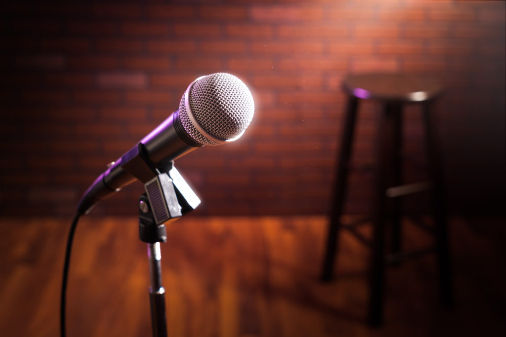 Microphone on a stage in front of a brick wall with a wooden stool out of focus in the background