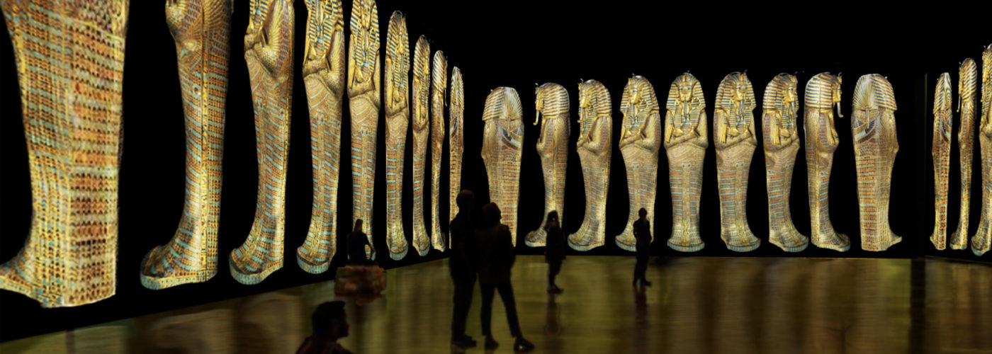Images from inside the Beyond King Tut: The Immersive Experience, showing silhouettes of people looking at projections of sarcophagi lining the walls