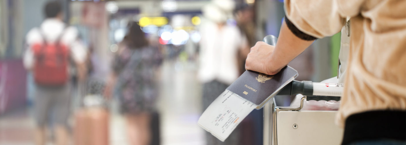 Close up of woman holding a boarding pass and passport while pushing a cart through an airport