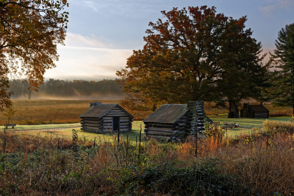Log cabins surrounded by a misty field and fall foliage at Valley Forge National Historical Park, Pennsylvania