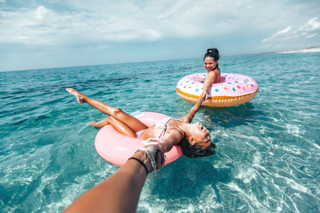 Woman in pool floats in the ocean holding hands