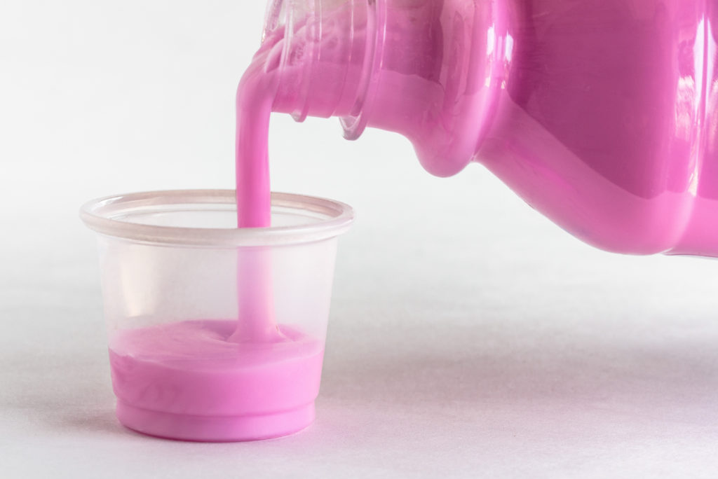 Pink antacid liquid being poured from a bottle into a small plastic cup