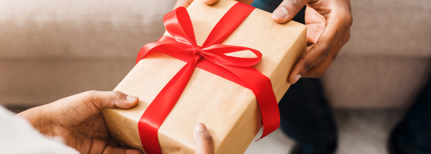 Close up of person handing wrapped gift with a red holiday ribbonto another person