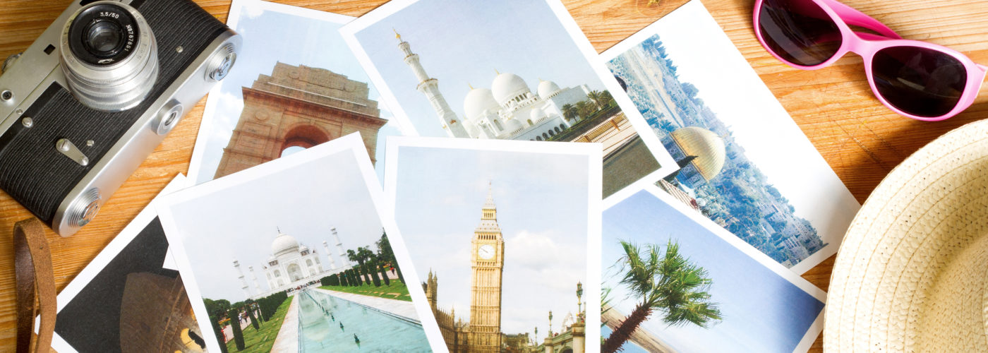 Printed travel photos surrounded by suitcase, sunglasses, and camera