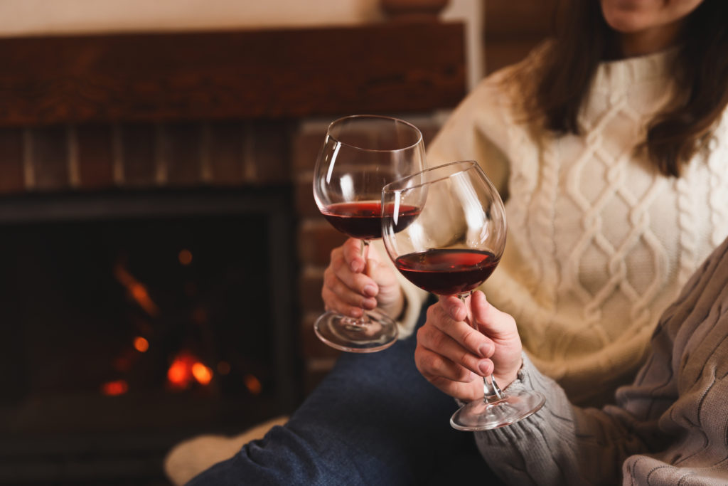 Close up of couple clinking glasses of red wine together in front of a fire
