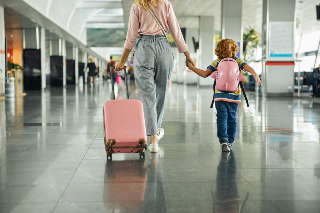 Woman holding hands with child and wheeling suitcase through airport