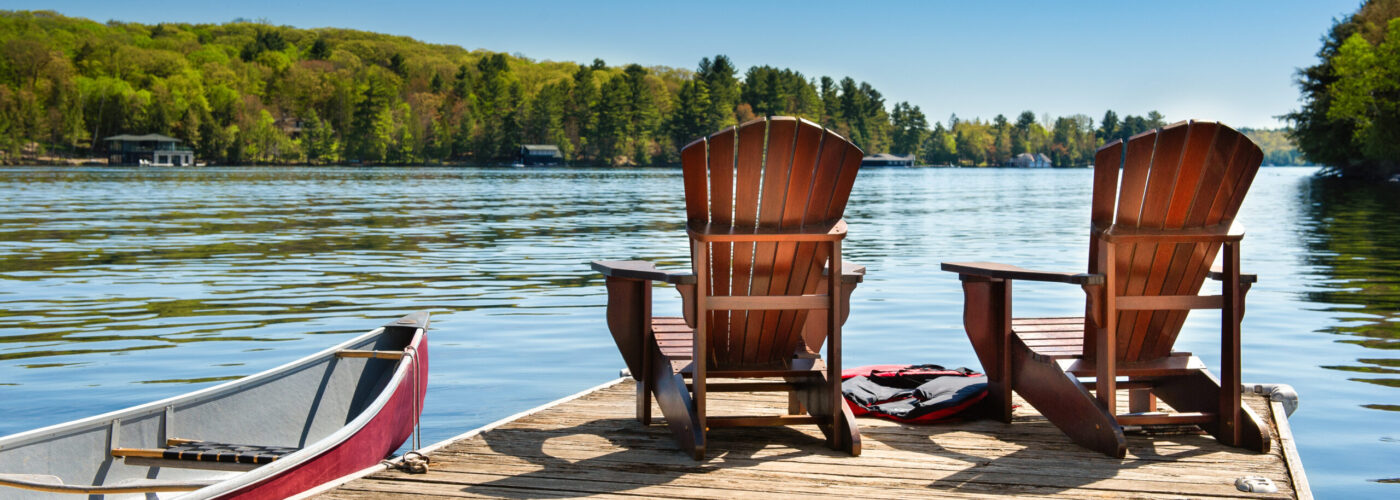 Two Adirondack chairs sitting on a dock overlooking a lake