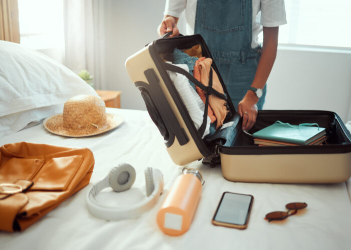 Person packing a hardside suitcase with travel gear on their bed