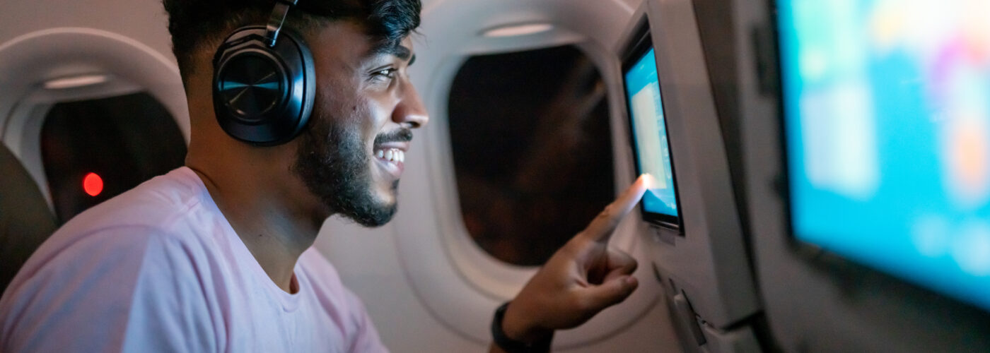 Man wearing bluetooth headphones scrolling through the menu of a seatback screen in an airplane